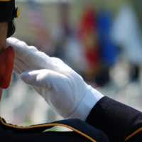 Military man saluting while wearing dress white gloves at a cemetery