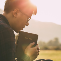 man praying with Bible in hand and a mountain in the background
