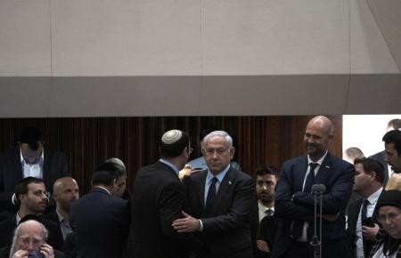 Israeli Prime Minister Benjamin Netanyahu embraces lawmaker Simcha Rothman on the floor of the Knesset, as people mass outside to protest his government's plan to overhaul the judicial system, Monday, March 27, 2023. (AP Photo/Maya Alleruzzo).