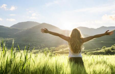 woman facing the mountains and sunshine with arms wide open