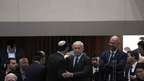 Israeli Prime Minister Benjamin Netanyahu embraces lawmaker Simcha Rothman on the floor of the Knesset, as people mass outside to protest his government's plan to overhaul the judicial system, Monday, March 27, 2023. (AP Photo/Maya Alleruzzo).