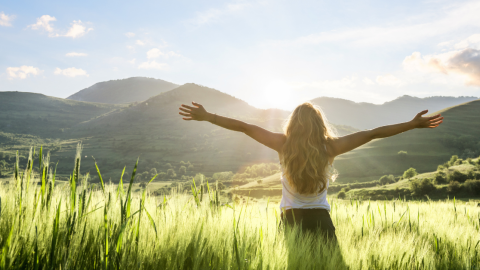 woman facing the mountains and sunshine with arms wide open